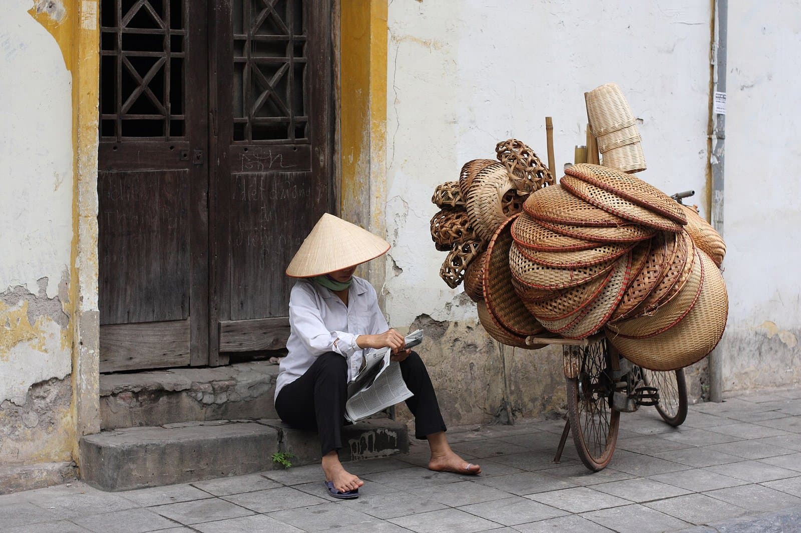 戴斗笠的小販坐在老屋門前,旁邊腳踏車掛滿竹籃